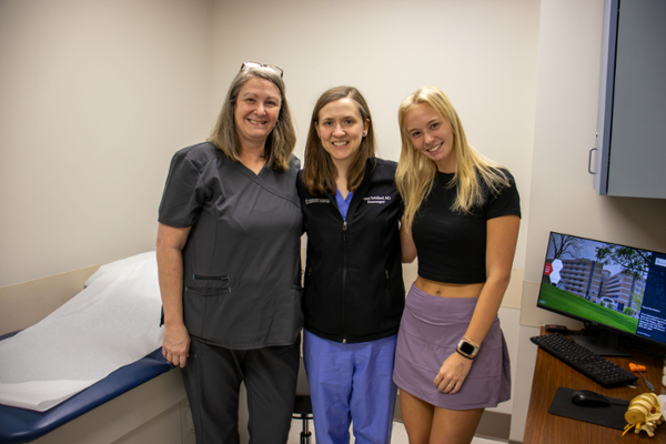 A mother and daughter standing with surgeon smiling in exam room.